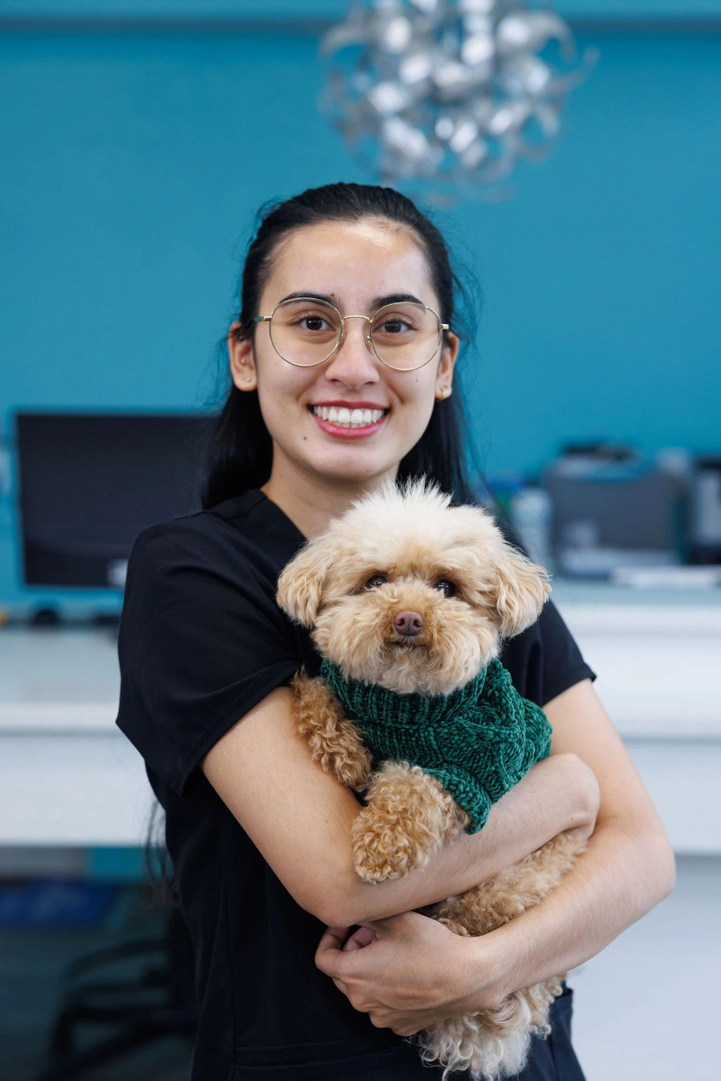 Emma holding a curly apricot toy poodle in a green sweater