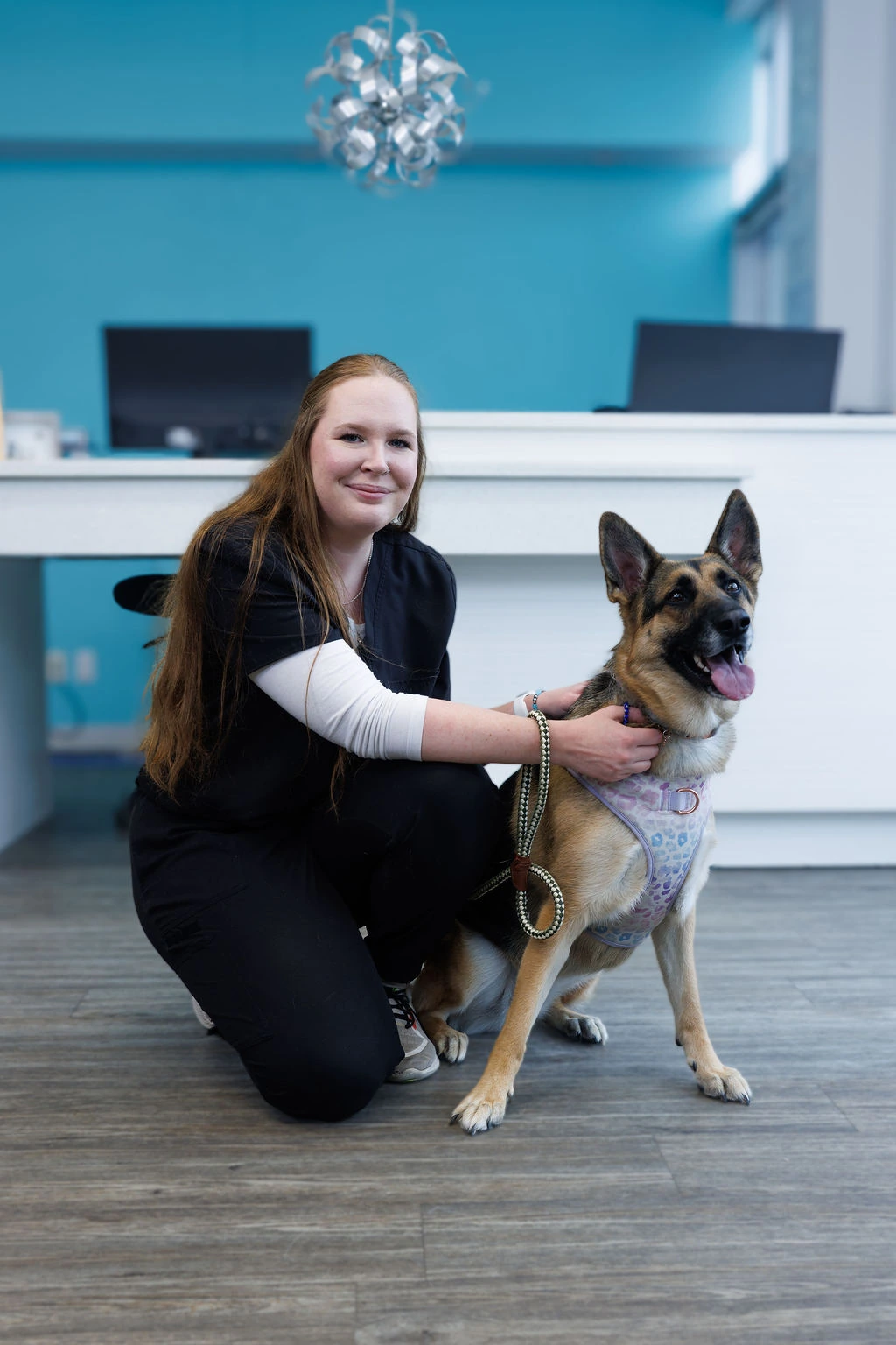 Keeley kneeling beside a German shepherd in a pastel harness